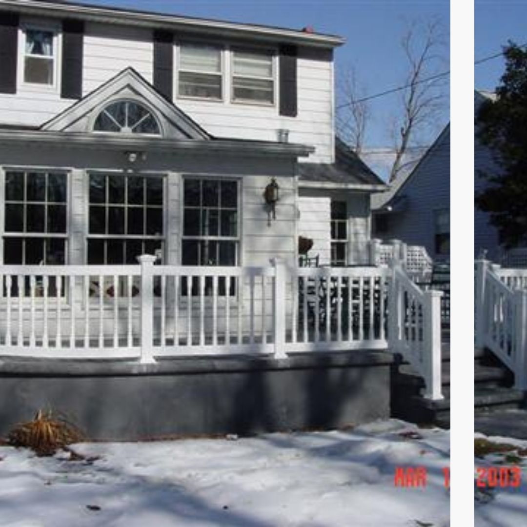 A white two-story house with a prominent front porch and white railings stands in a snowy landscape under a clear sky.