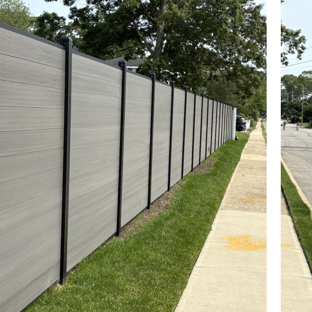 A newly installed grey composite privacy fence with modern black posts and top rails, bordering a sidewalk