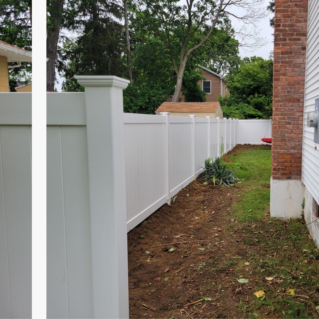 A long, white vinyl privacy fence with decorative post caps, freshly installed along a residential property line next to a brick house